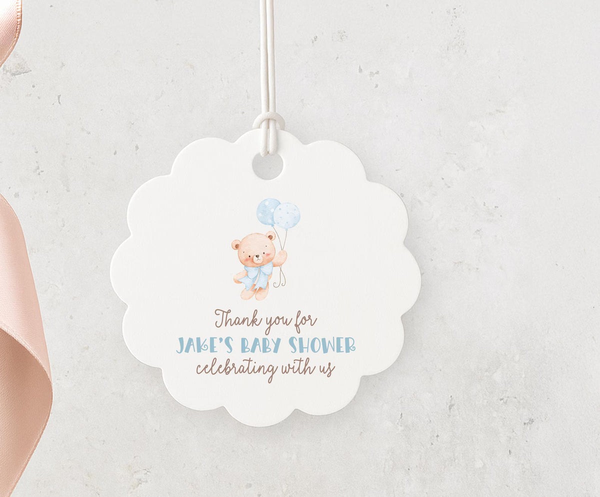 A white scalloped tag with a teddy bear and balloons, hanging on a string.
