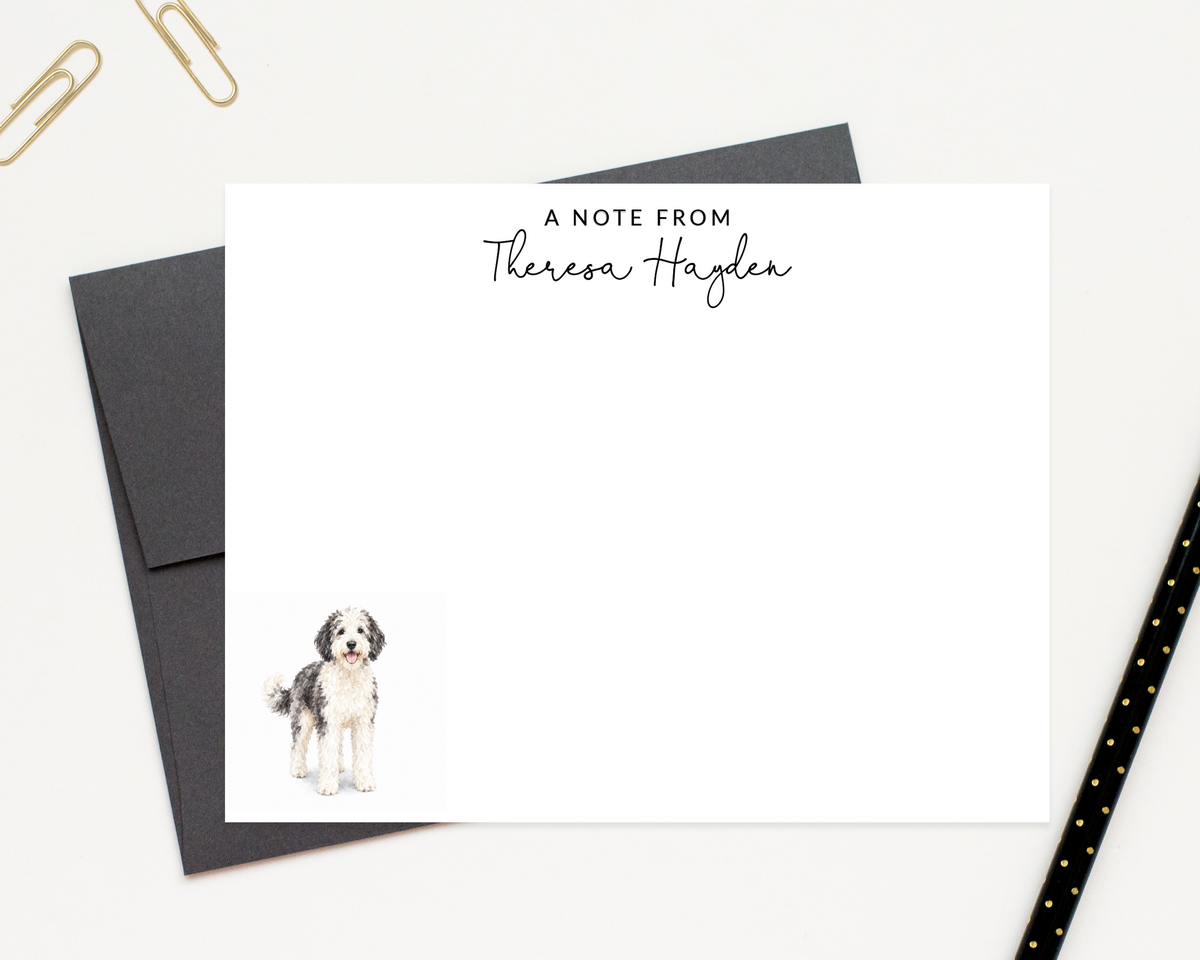 a personalized note card with a dog illustration on it, placed on a desk with a black envelope and a black pen.