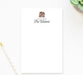 a blank white card with a personalized message and a coat of arms, placed on a white surface next to a pen and a small plant.