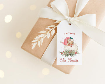 A gift wrapped in brown paper with a white ribbon and a Santa Claus tag attached to it.