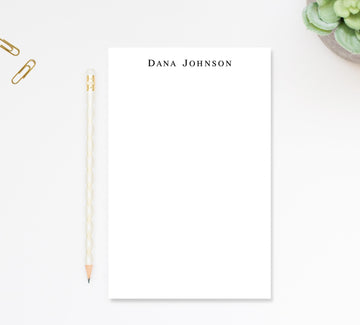 a blank white notepad with the name 'Dana Johnson' written on it, accompanied by a pencil and a small plant.