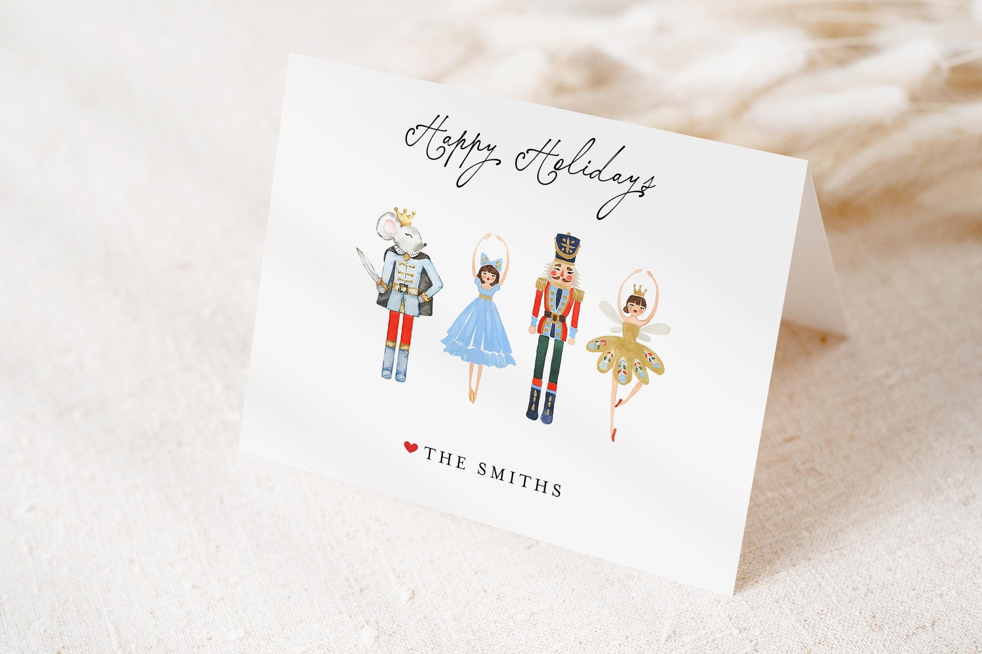A greeting card featuring four illustrated characters in costumes, including a nutcracker, a mouse, a ballerina, and a fairy. The card has a "Happy Holidays" message and the name "The Smiths" printed on it.