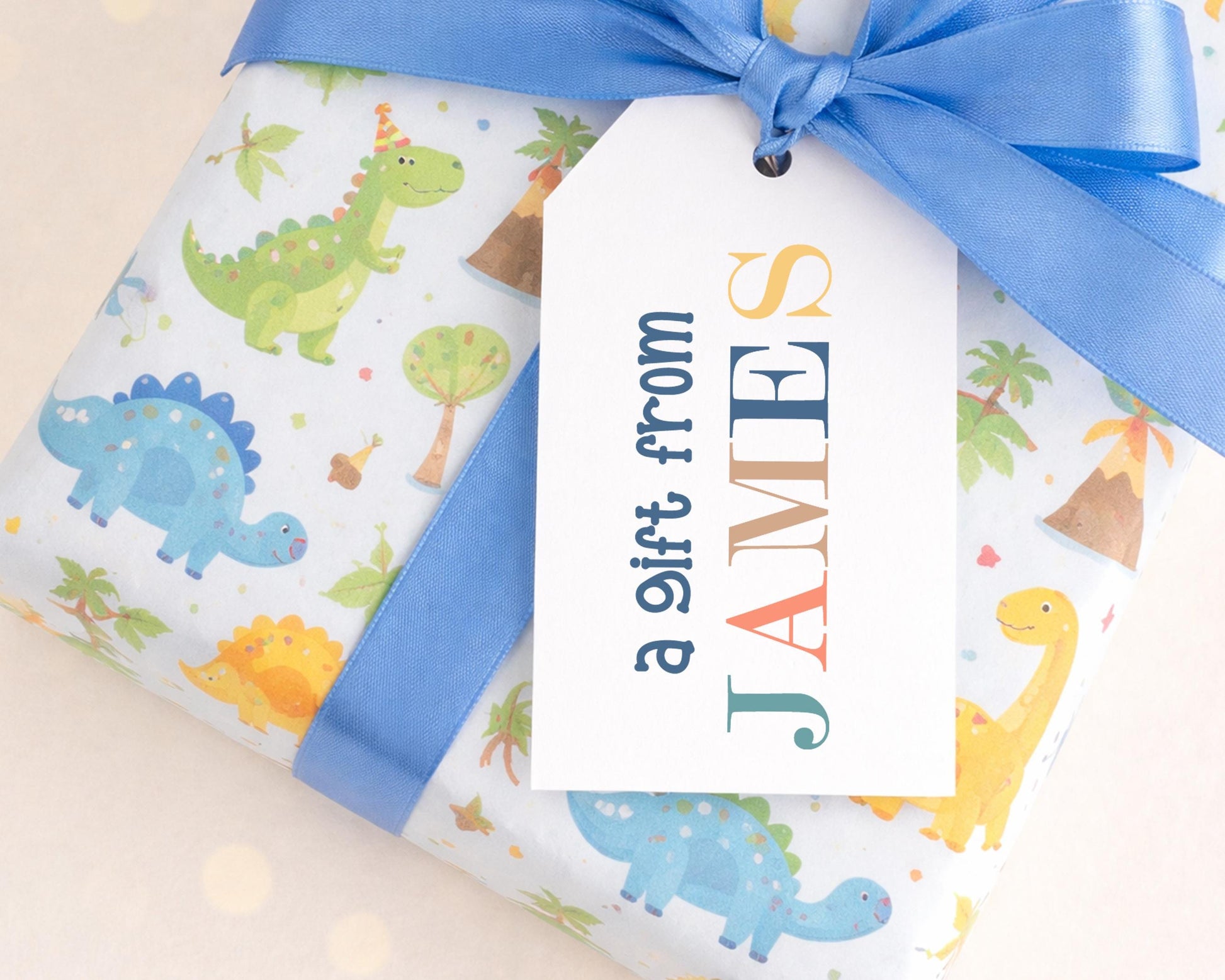 A gift wrapped in a dinosaur-themed wrapping paper with a blue ribbon, featuring a personalized gift tag that reads "a gift from JAMES".