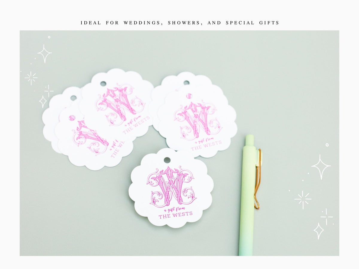 three white paper tags with pink monogrammed designs, a green pen, and a light blue background with white stars.