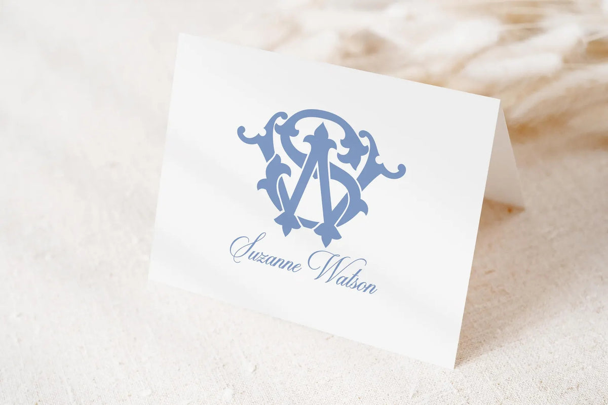 A white card with a blue monogram logo and the name "Suzanne Watson" printed on it.