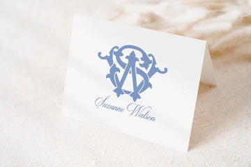 A white card with a blue monogram logo and the name "Suzanne Watson" printed on it.