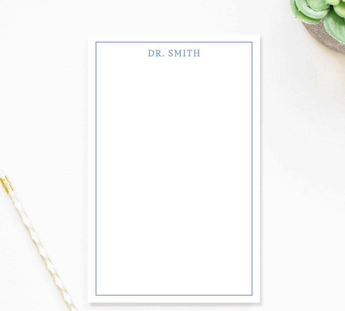 a blank white notepad with a blue border, placed on a white surface next to a pen and a small green plant.