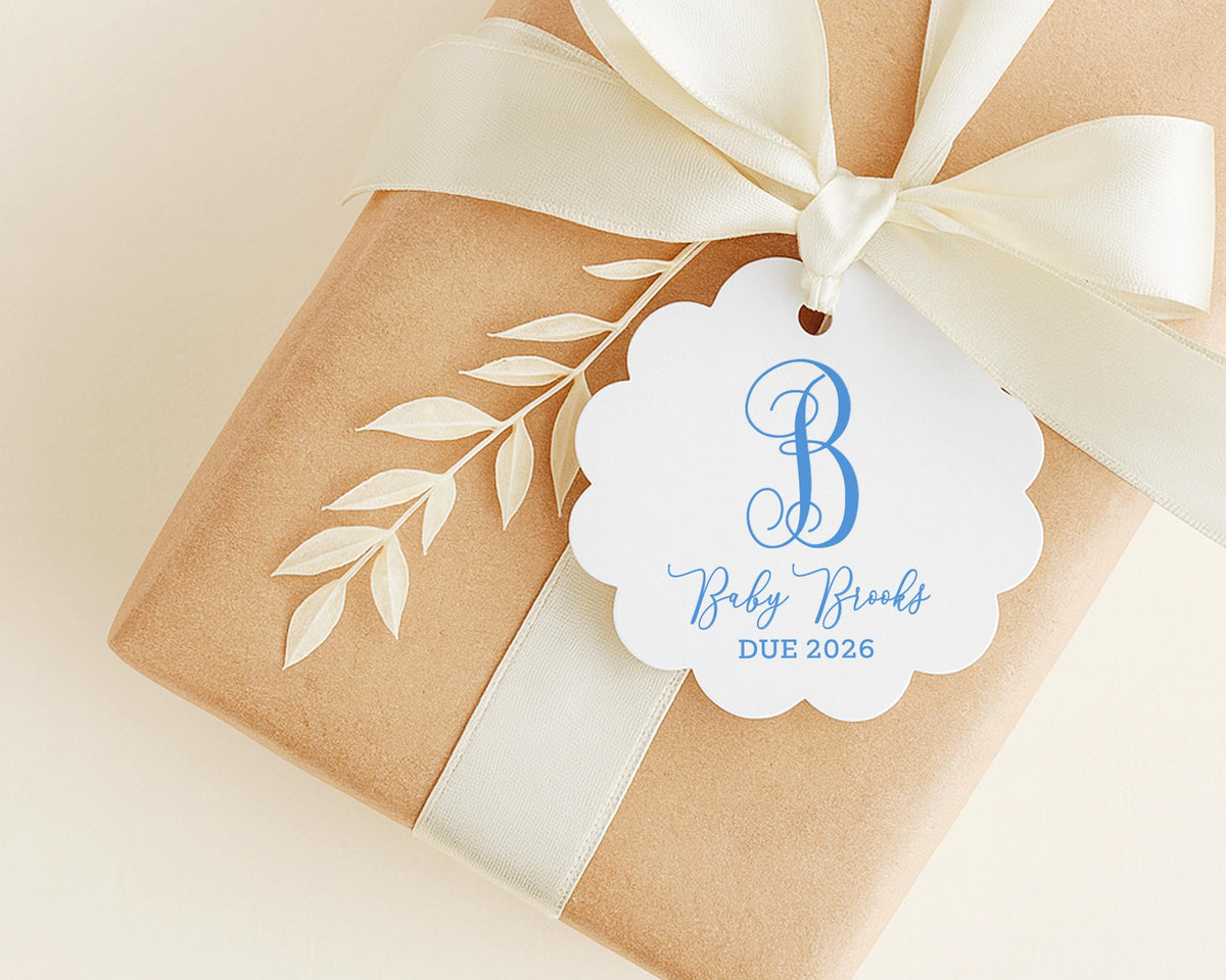A brown gift box with a white ribbon and a white tag with a blue letter "B" and text that reads "Baby Brooks DUE 2026".
