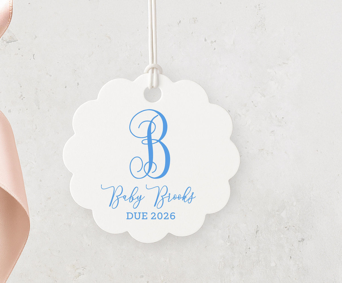 A white scalloped tag with a blue monogram and text, hanging on a string.