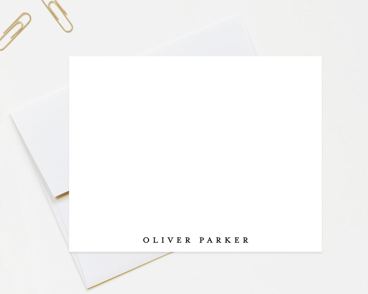 a blank white card with the name "OLIVER PARKER" printed on it, along with a pair of gold-colored paper clips placed on a white surface.