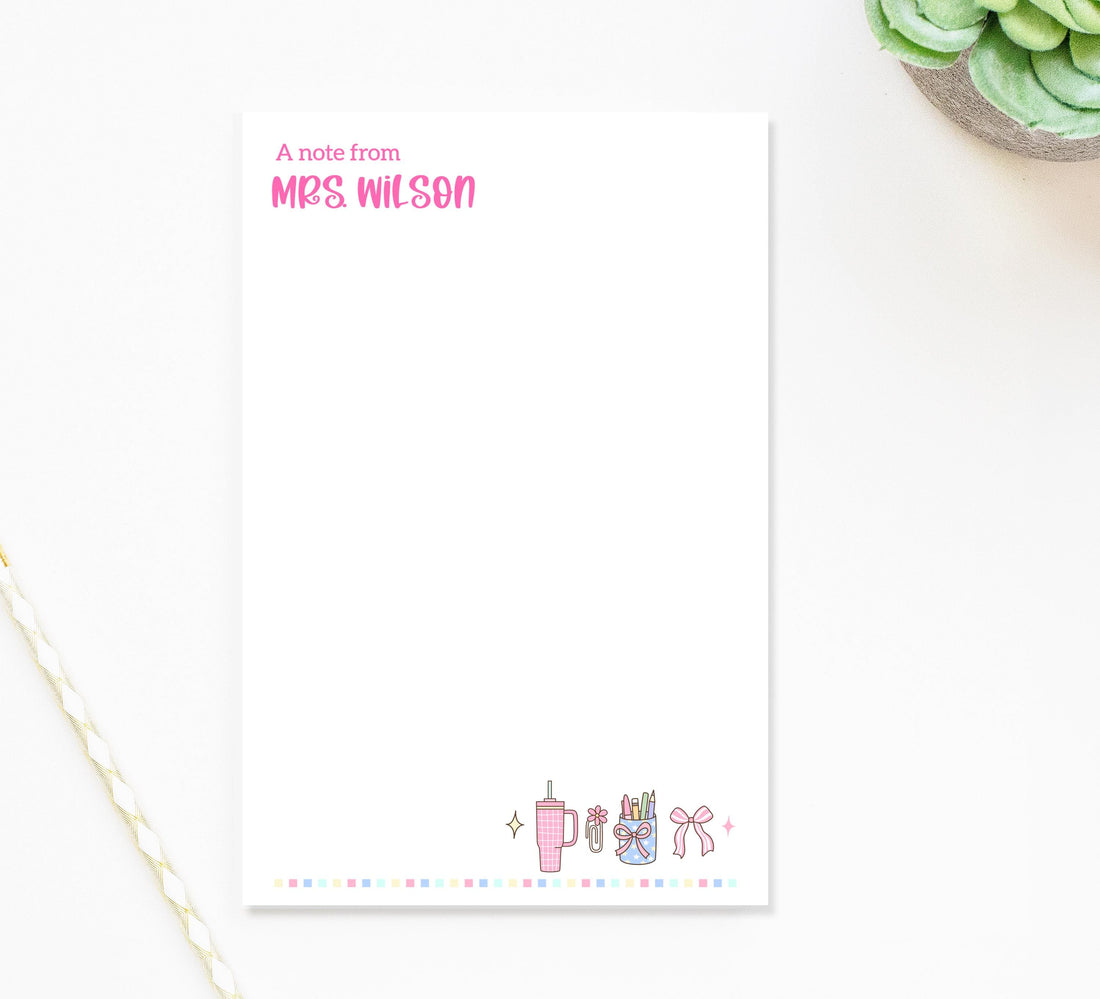 A blank white notepad with a personalized note from Mrs. Wilson printed on it, along with a decorative border featuring various objects such as a cup, pencils, and a plant.