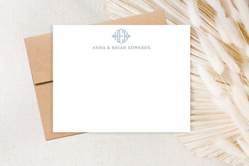 a blank white card with a monogrammed logo, placed on a brown envelope, with a decorative beige leaf in the background.